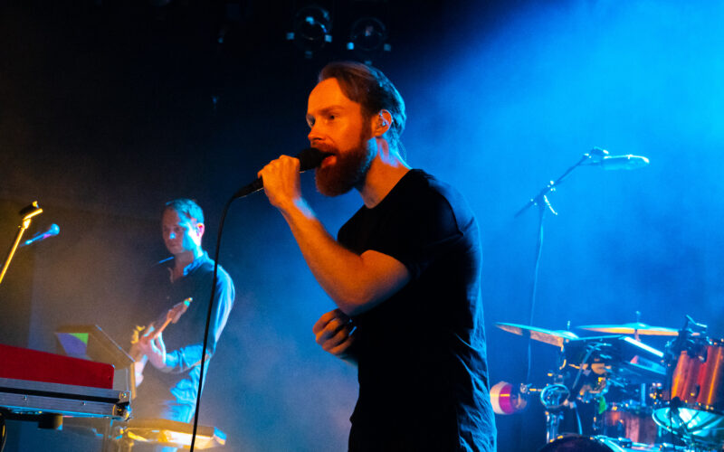 Enno Bunger bei einem Konzert, in der linken Hand hält er ein Mikrofon, links neben ihm ist im Hintergrund ein Gitarrist zu sehen.