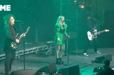 Lauren Mayberry und Robert Smith stehen gemeinsam auf der Bühne und tragen How Not To Drown vor. Lauren trägt ein grünes Kleid, ebenso ist die Bühne in grünes Licht getaucht.
