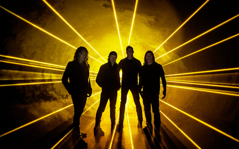 Die Band Metallica. Die vier Männer stehen vor einem gleißenden, gelben Licht, dessen Strahlen hinter ihnen hervorkommen. Sie sind vor allem schemenhaft zu erkennen.