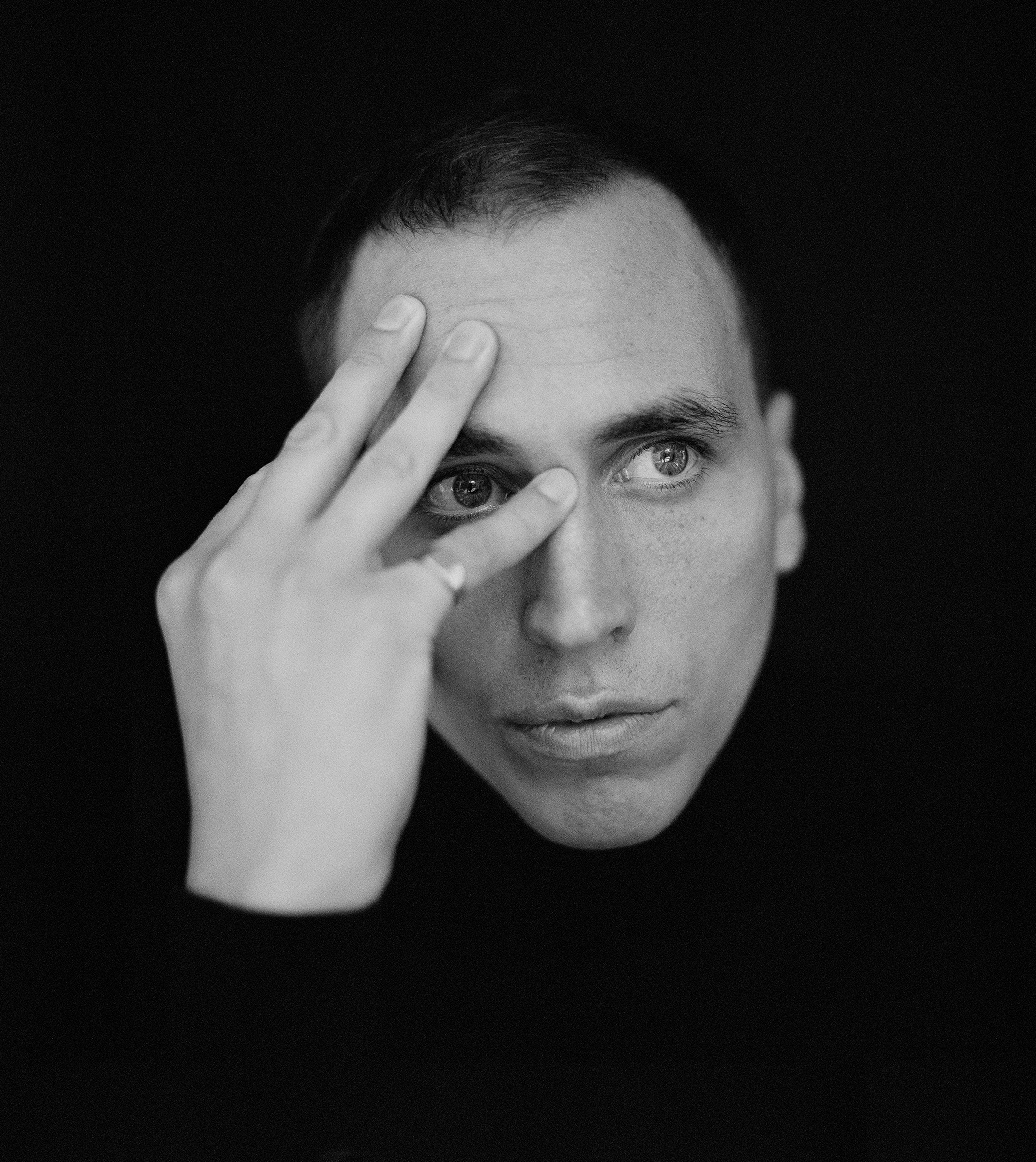 Schwarzweißes Portraitfoto von Martin Kohlstedt. Man sieht nur sein Gesicht sowie die rechte Hand, die er sich an die Stirn hält und damit Teile seines Gesichts halb verdeckt.